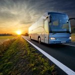 Bus driving on a road at sunset.