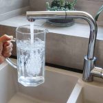 Hand filling pitcher with water from faucet.