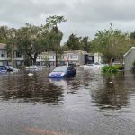 Flooded residential area with partially submerged cars and buildings.