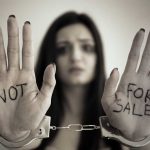 Handcuffed woman shows "NOT FOR SALE" on her palms.