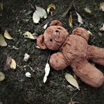 Teddy bear on grass with fallen leaves.
