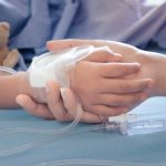 Child's hand with IV, held by adult.