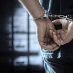 Person in handcuffs standing in dimly lit room.