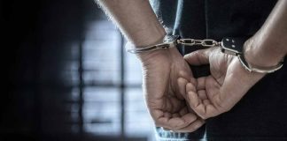Person in handcuffs standing in dimly lit room.