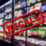 "Recall" stamp over blurred grocery store shelves.