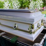 White coffin with flowers in the background.