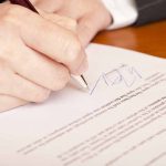 Hand signing a document on a wooden table