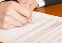 Hand signing a document on a wooden table
