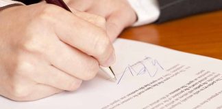 Hand signing a document on a wooden table