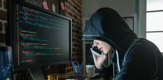 Hacker in hood using computer and phone analyzing code