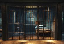 Empty prison cell with metal bars and bed.
