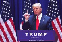 Man speaking at podium with USA flags behind him