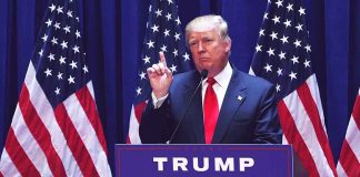 Man speaking at podium with USA flags behind him