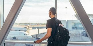 Person with backpack at airport window watching airplanes