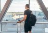 Person with backpack at airport window watching airplanes