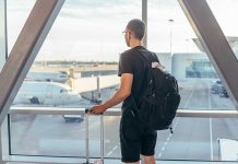 Person with backpack at airport window watching airplanes