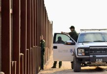 Border patrol agents near a tall metal fence