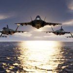 Five fighter jets flying over the ocean at sunset.
