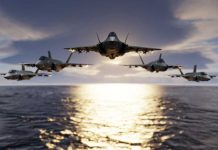 Five fighter jets flying over the ocean at sunset.