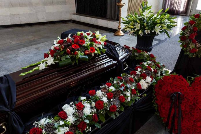 1869583603 featured image Funeral casket surrounded by red and white flowers.