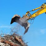 Excavator demolishing rubble against a blue sky.