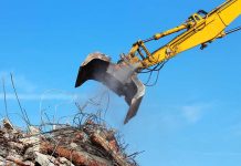 Excavator demolishing rubble against a blue sky.