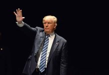 Man in a suit waving against dark background