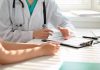 Doctor discussing with patient holding clipboard on desk