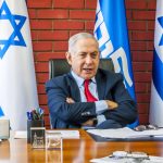 Man sitting at desk with Israel flags behind him