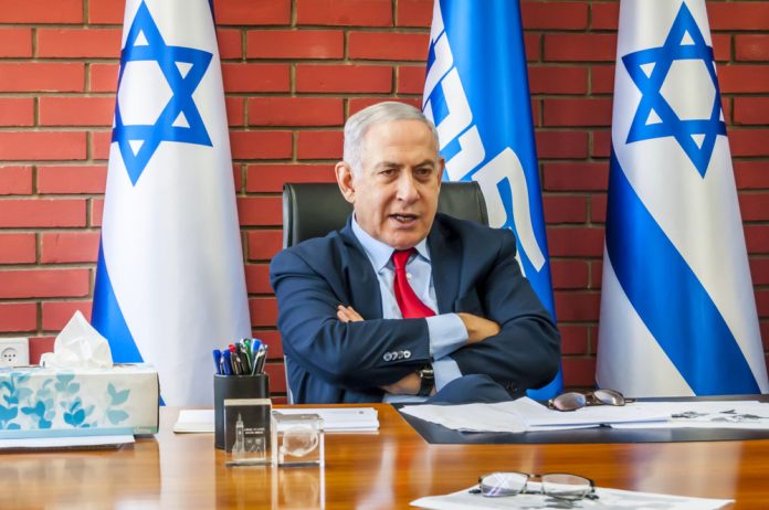 1564752907 featured image Man sitting at desk with Israel flags behind him