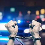 Hands in handcuffs in front of police cars