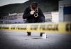 Crime scene photographer behind police tape with evidence marker