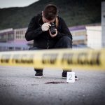 Crime scene photographer behind police tape with evidence marker