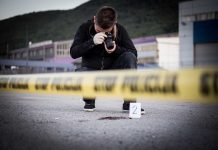 Crime scene photographer behind police tape with evidence marker