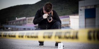 Crime scene photographer behind police tape with evidence marker