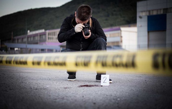 Crime scene photographer behind police tape with evidence marker