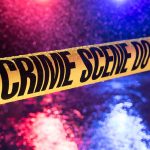 Yellow crime scene tape with police lights in background