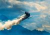 Helicopter releasing smoke over mountainous landscape with clouds