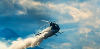Helicopter releasing smoke over mountainous landscape with clouds