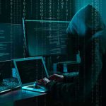 Hacker in dark room surrounded by computer screens