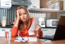 Woman looking stressed holding bills in kitchen