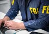 Person in FBI jacket typing on a laptop
