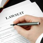 Hand holding pen, filling out lawsuit form.