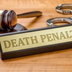 Gavel, handcuffs, and Death Penalty sign on desk.