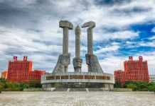 Concrete monument with hands holding tools under cloudy sky