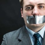 Man in business attire with duct tape over his mouth, conveying a message about silence