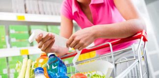 Person holding a shopping list while looking at groceries in a cart