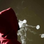 Person in red hoodie blowing smoke rings.