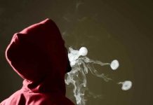 Person in red hoodie blowing smoke rings.