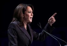 Person speaking at podium with raised finger.
